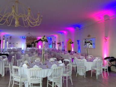 Salle de réception décorée avec des tables blanches et un éclairage coloré.